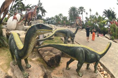 CHON BURI, THAILAND - SEPT 5, 2023: Kimliği belirsiz turistler, Nong Nooch Tropikal Bahçesi 'ndeki Dinozor Vadisi' nde çeşitli boyutlarda bir dinozor heykelini ziyaret ediyorlar..