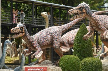 CHON BURI, THAILAND - SEPT 5, 2023: Kimliği belirsiz turistler, Nong Nooch Tropikal Bahçesi 'ndeki Dinozor Vadisi' nde çeşitli boyutlarda bir dinozor heykelini ziyaret ediyorlar..