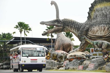 CHON BURI, THAILAND - 6 Eylül 2023: Nong Nooch Tropikal Bahçesi 'ndeki Dinozor Vadisi' ndeki çeşitli boyutlardaki güzel dinozor heykellerinde turist otobüsü, başka bir büyük turistik ilgi alanı..
