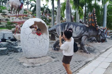 CHON BURI, THAILAND - 24 Eylül 2023: Nong Nooch Tropikal Bahçesindeki Dinozor Vadisi 'nde dinozor yumurtası heykelleriyle fotoğraf çeken turistlerin kimliği belirlenemedi.