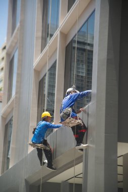 BANGKOK, THAILAND- 11 AUG 2024: İşçiler gökdelen binasının camlarını temizliyor. Pencere temizleyicileri modern binaların cam temizleme sınıfını temizliyorlar. Güvenlik halatıyla yukarıdan aşağıya süzülüyor.