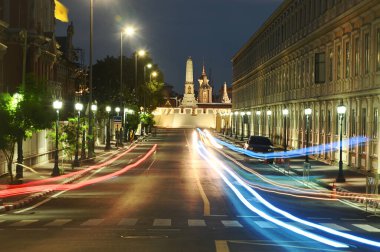 Her iki tarafta da çalışan arabaların olduğu yol devlet binaları. Alacakaranlıkta Wat Phra Kaew surlarına doğru gidiyor. Tayland 'ın Bangkok şehrinde..