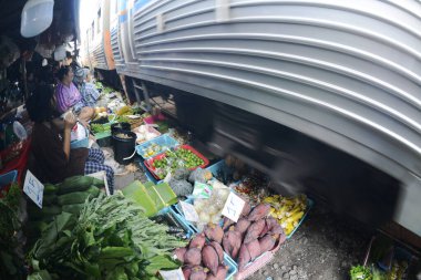SAMUT SAKHON, THAILAND- 29 SEPT 2024: İsimsiz bir satıcı Mahachai İstasyonu 'nda tren yolu boyunca sebze, meyve ve çiçek satıyor. Tren geldiğinde, rafları yerinde bırakıyor çünkü daha aşağıda....