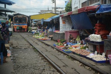 SAMUT SAKHON, THAILAND- 29 SEPT 2024: İsimsiz bir satıcı Mahachai İstasyonu 'nda tren yolu boyunca sebze, meyve ve çiçek satıyor. Tren geldiğinde, rafları yerinde bırakıyor çünkü daha aşağıda....