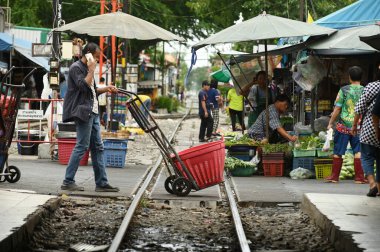 SAMUT SAKHON, THAILAND - 9 Eylül 2024: Meçhul bir Asyalı erkek, Mahachai Tren İstasyonu 'ndaki bir el arabasında sebze ve eşyaları varış noktasına kadar plastik bir sepete koyar.