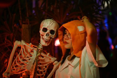 CHACHOENGSAO, THAILAND - ECTOBER 2024: Kimliği belirsiz güzel bir turist mutlu ve sevinçli bir şekilde Somdej Phra Srinakarin parkındaki 2. Cadılar Bayramı etkinliğinde korkunç bir iskeletle fotoğraf çekiyor..