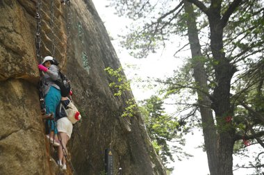 SHAANXI, THAILAND - 20 Haziran 2023: Tanımlanamayan turistler dik taş basamaklara tırmanıyor ve Huashan Dağı 'nda asılı kalıyorlar. Çin' in en ünlü turistik yerlerinden biri de kaya tırmanışı ve yürüyüş faaliyetleri.. 