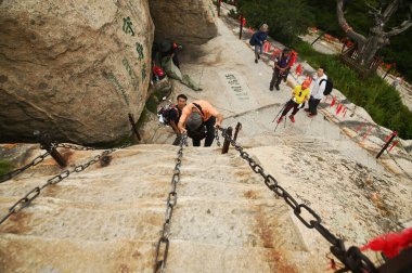 SHAANXI, ÇİN - 20 Haziran 2023: Tanımlanamayan erkek turistler dik taş basamaklara tırmanıyor ve Huashan Dağı 'nda sallanan zincirler Çin' in en ünlü turistik yerlerinden biri..