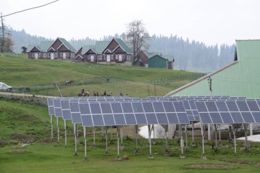 JAMMU AND KASHMIR , INDIA - MAY 10 , 2019 : Field with rows of solar panels in grassland and village background in Gulmarg , Jammu-Kashmir,India.