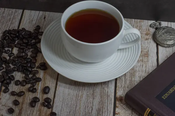 Kavrulmuş kahve çekirdekleri, eski bir cep saati ve deri ciltli bir kitapla çevrili, sade, sade bir kahve bardağının yakın çekimi. Rahat bir sabah atmosferi, rahatlamak için mükemmel, ve kafein aşıkları