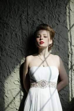 Çarpıcı beyaz elbisesi ve kalın kırmızı dudakları olan kendine güvenen bir kadın büyüleyici bir pozda zarafet saçar.