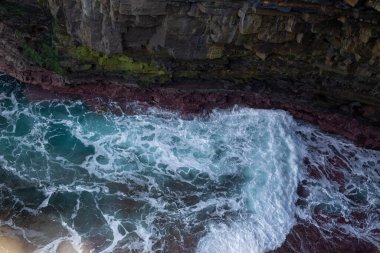 Çarpıcı bir hava manzarası kayalık kıyı şeridine çarpan muhteşem dalgaları gösteriyor, canlı renkleri ortaya çıkarıyor.