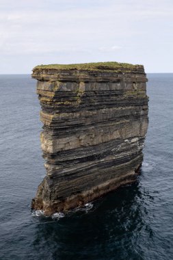 Okyanustan çarpıcı bir dikey kaya oluşumu yükseliyor ve jeolojik tarihin birçok katmanını ortaya çıkarıyor.