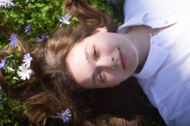 Huzurlu genç bir kadın dingin kır çiçeklerinin arasında huzur ve neşe saçan bir tarlada dinleniyor.