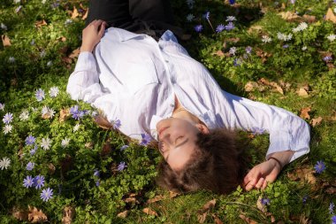 Huzurlu bir sahnede, bir insan yemyeşil bir ortamda güzel bir çiçek dizisinin arasında huzur içinde dinlenir.