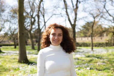 Neşeli ve hayat dolu bir kadın rengarenk çiçeklerle dolu canlı bir bahar manzarasında kendine güvenerek poz verir.