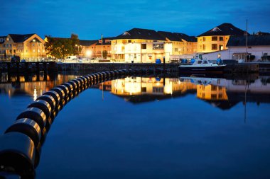 Gün batımında sakin sulara yansıyan canlı ışıkların yer aldığı güzel ve pitoresk bir liman sahnesi.