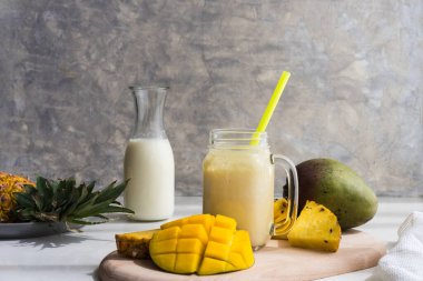 Sağlıklı mango ve ananas suyu gri arka planda cam bir kavanozda.