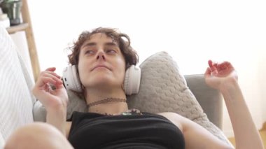 Kadın kanepede dinlenirken kulaklıkla müzik dinliyor.