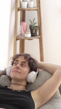 Kadın kanepede dinlenirken kulaklıkla müzik dinliyor.