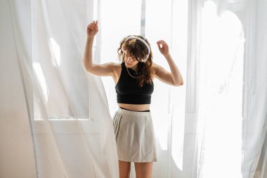 Kadın kulaklıkla müzik dinlerken pencerenin önünde dans ediyor..