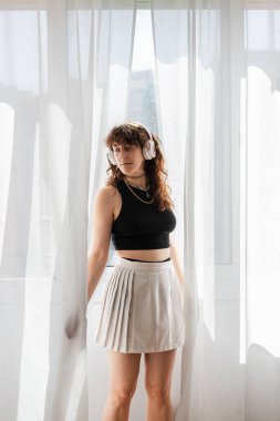 Kadın kulaklıkla müzik dinlerken pencerenin önünde dans ediyor..