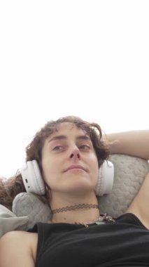 Kadın kanepede dinlenirken kulaklıkla müzik dinliyor.
