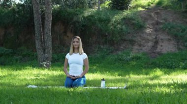 Yoga minderinde oturmuş parkta meditasyon yapan genç bir kadın.