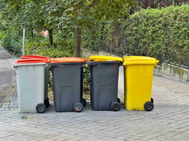 Kaldırıma dizilmiş dört çöp tenekesi var. Çöp tenekeleri farklı renk ve boyutlarda.