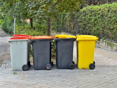 Kaldırıma dizilmiş dört çöp tenekesi var. Çöp tenekeleri farklı renk ve boyutlarda.