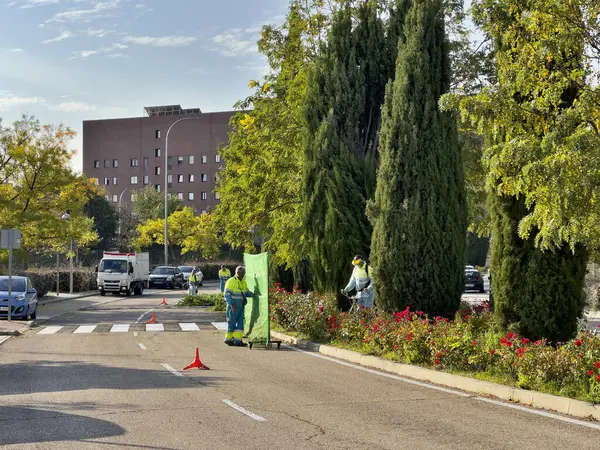 Güvenlik donanımlı işçiler ağaçlar ve çiçeklerle döşenmiş bir karayolu ortamını koruyorlar.