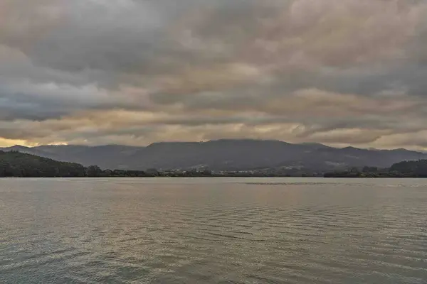 Sakin suları olan sakin bir göl manzarası bulutlu gökyüzünü yansıtıyor. Arka planda dağlar görülebiliyor ve sakin bir atmosfer yaratıyorlar. Sahne alacakaranlıkta çekilir, sessiz renkler ve yumuşak lig