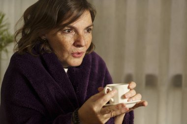 Sıcak bir içeceğin tadını çıkaran düşünceli kadın.