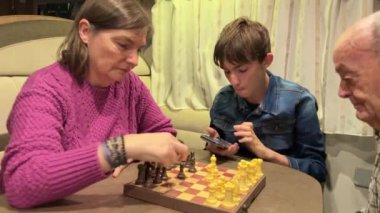 Aile üyeleri bir satranç tahtasının etrafında toplanıp oyun oynuyorlar ve bir karavanın rahat atmosferinde kaynaşıyorlar.