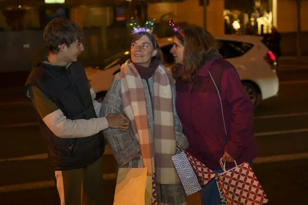 Parlak ren geyiği boynuzlu mutlu bir aile. Saç bandı, alışveriş torbaları taşıyor ve Noel tatili boyunca bir şehir caddesinde yürüyor.