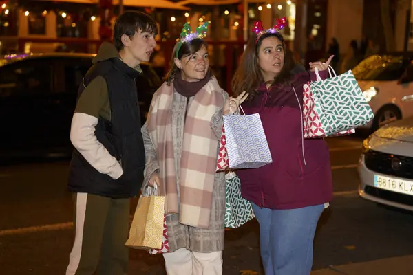 Noel bandı takan aile, alışveriş torbaları taşıyor ve geceleri şehirde Noel alışverişinin keyfini çıkarıyor.