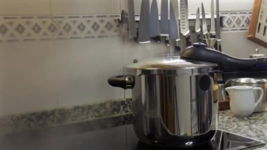 Profesyonel aşçı, düdüklü tencere kapağını emniyete alıyor mutfak tezgahında hassasiyetle yemek hazırlıyor yemek pişirme tekniğini ve mutfak güvenliğini gösteriyor.