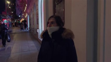 Gran Via gece şehir manzarasında şık giyimli bir kadın aydınlanmış kentsel kış atmosferinin ortasında duruyor ve festival sezonunda Madrid 'in ikonik caddesini izliyor.