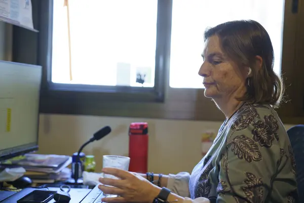 Konforlu bir ofis ortamında bilgisayar üzerinde çalışırken bir bardak dinlendirici suyun keyfini çıkaran odaklanmış bir çalışan.