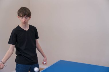 Genç adam masa tenisini içeride oynuyor. Yeteneklerini geliştirmeye ve antrenman sırasında tekniğini mükemmelleştirmeye odaklanıyor.