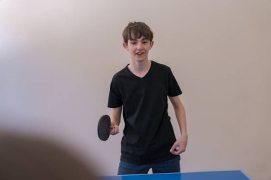 Genç adam raket ve topu kavrıyor, yoğun masa tenisi maçı için hazırlanıyor, yeteneğini ve konsantrasyonunu gösteriyor.