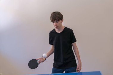 Gençler masa tenisi çalışıyor, beyaz bir duvarın önünde mavi bir masada raketle topu sektiriyorlar.