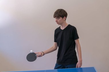 Masa tenisi antrenmanı yapan genç bir adam, kapalı bir ortamda mavi masaya odaklanırken ustalıkla raketinin üzerinde top sektiriyor.