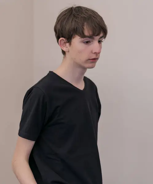 Kahverengi saçlı, siyah tişörtlü, üzgün ve utangaç bir gencin portresi.