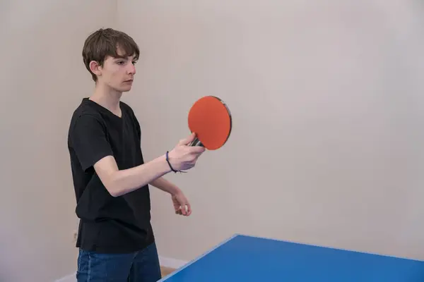 Genç, canlı mavi bir masada masa tenisi oynuyor, topun zıplamasını, odaklanmasını ve antrenman sırasında atletizm göstermesini hevesle bekliyor.