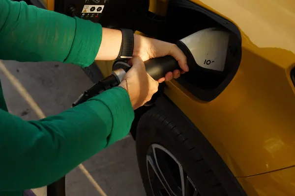 Şarj istasyonunda şarj kablosunu sarı elektrikli araca bağlayan ellerin yakın çekimi sürdürülebilir ulaşımı gösteriyor