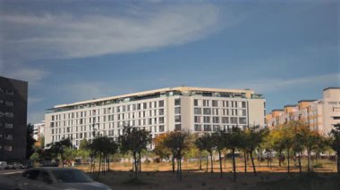 Hareket halindeki bir araçtan görülen çağdaş konut binaları. Güneşli bir günde modern mimari, ağaçlar ve geçen arabalarla şehir manzarası