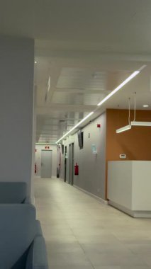 Boş bir hastane ya da klinik koridorunun modern ve temiz iç mekanı. Resepsiyon masası, bekleme odası sandalyeleri ve muayenehanesi olan uzun koridor.
