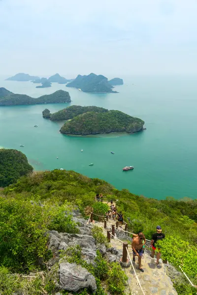 Tayland 'daki Mu Ko Ang Tanga Ulusal Deniz Parkı' nda çekilen bu fotoğraf, yemyeşil bir araziyle çevrili kayalık bir yolda yürüyen bir grup insanı gösteriyor. Arkaplan turkuaz suları ve küçük adaları gözler önüne sererek takımadaların panoramik manzarasını sunuyor..