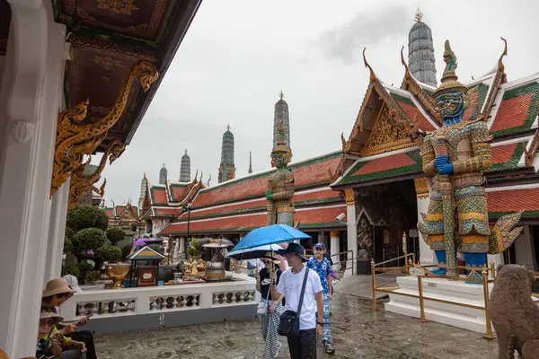 Şemsiyeli ziyaretçiler, Tayland 'ın Bangkok kentindeki Büyük Saray kompleksinde bulunan Zümrüt Buda Tapınağı olarak da bilinen Wat Phra Kaew' i keşfediyorlar. Sahne tapınağın ikonik mimarisini ve canlı koruyucu heykellerini yakalıyor..